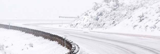 A snowy road with a fence on the side of it.